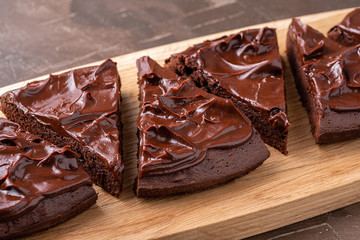 Serving triangular brownie with ganache cream on a serving wooden board. Close up.