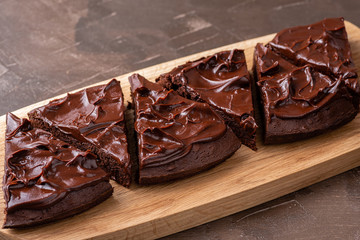 Serving triangular brownie with ganache cream on a serving wooden board. Close up.