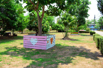 the colorful wooden stall with heart shape around the tree at the yard with dry grass on ground in summer