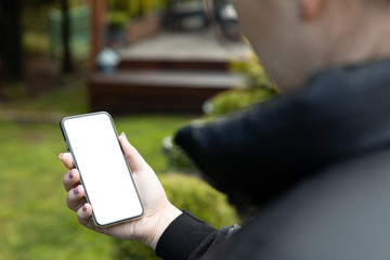 Woman is holding a smartphone with blank frameless screen on the background of the garden