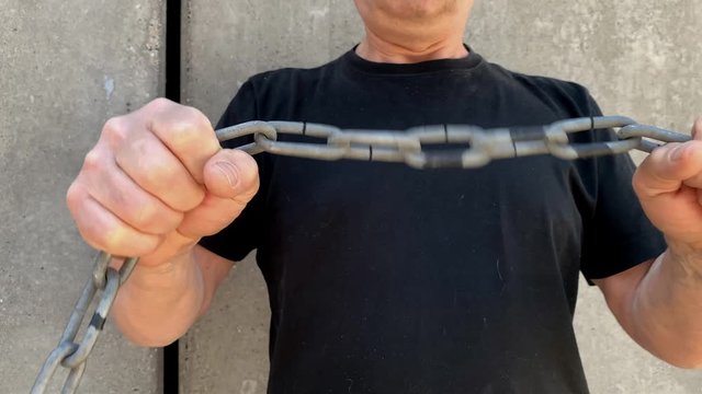 strong man holds thick iron chains in his hands, yanks them, tries to break the steel, the concept of strength, fetters, bondage, conclusions