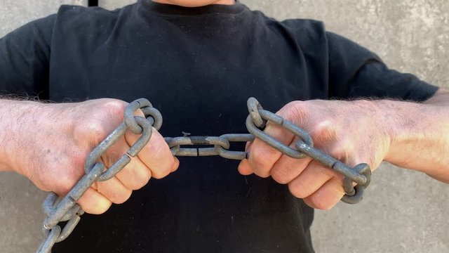 strong man holds thick iron chains in his hands, yanks them, tries to break the steel, the concept of strength, fetters, bondage, conclusions