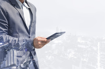 double exposure business man hands use tablet smartphone typing on screen for working with technology wireless communication connection with cityscape building background.