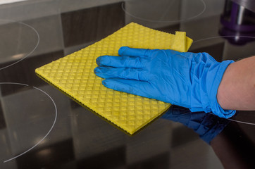 Housekeeper in protective gloves washes the induction cooker with a yellow rag