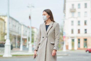 A brunette girl with long hair in a medical face mask to avoid the spread coronavirus holds a...