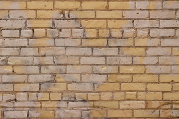 Grungy old yellow brick wall texture background showing severe weathering and areas of blotchy white faded paint