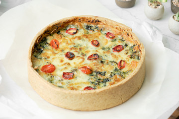 Homemade cheesy spinach quiche for brunch. set on white cafe table background.