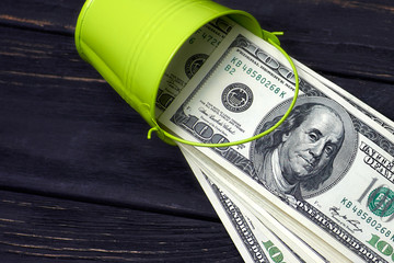 Green bucket of one hundred dollars banknotes on black wooden table. Selective focus. © zontica