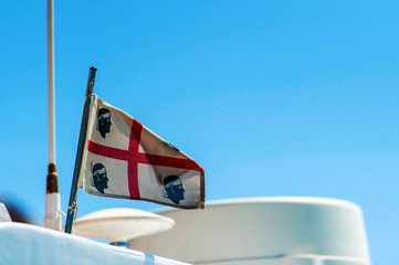 A view of a Sardinian flag blowing in the wind on top of a yacht with the blue sky in the background on a sunny day, in Sardinia Italy