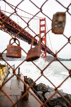The Golden Gate Bridge behind a fence line with rusted  locks hanging on it. 