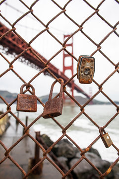 The Golden Gate Bridge behind a fence line with rusted  locks hanging on it. 