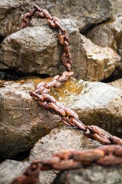 A rusted metal chain lying on top of wet rocks. 