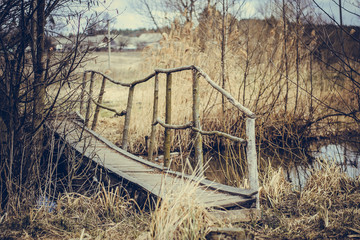 Old wooden bridge over the river in early spring. Gray-brown background. Old unpainted boards. Small river in the village. Late fall.