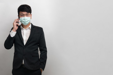 Asian businessman wear surgical face mask in formal black suit jacket, using smartphone to talking, look at the camera, studio lighting isolate with grey background, concept coronavirus, covid19