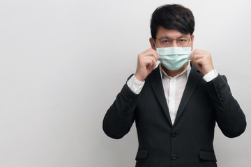 Asian businessman wearing surgical face mask in formal black suit jacket, two hands touch the mask and looking at the camera, studio lighting isolate with grey background, concept coronavirus, covid19