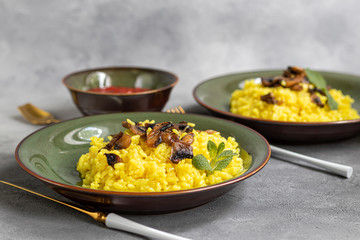 Italian risotto with champignons and parmesan on a gray background in dark plates. Rice is seasoned with turmeric and herbs.
