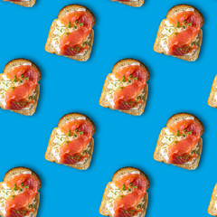 Seamless pattern sandwiches with red fish and cottage cheese sauce, sprinkled with greens. Healthy food flatlay in pop art style on a blue background.