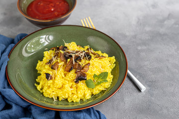 Italian risotto with champignons and parmesan on a gray background in dark plates. Rice is seasoned with turmeric and herbs.