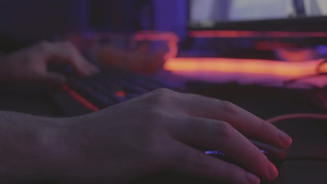 Close up of hands of unrecognizable computer games player using computer mouse and gaming keypad illuminated with neon light