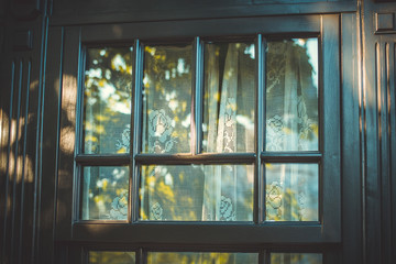 The wooden window is dark brown with an openwork white curtain. Retro window. Wooden frame. A small wooden window. The window of the cafe. Street reflection in a glass. Veranda.