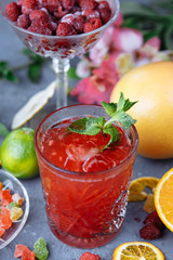 Fresh pink lemonade with raspberries decorated with mint leaves, orange, lime and candied fruit on a decorative background
