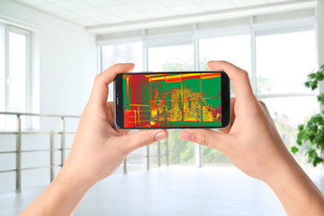 Woman detecting heat loss in room using thermal viewer on smartphone. Energy efficiency