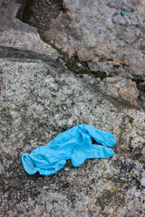 Used medical gloves on the stone. Blue crumpled disposable glove dumped on the ground pose public health risks and pollute the environment