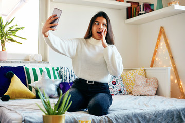 Urban fashion young girl holding cellphone and sitting on bed.