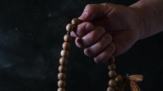 Wooden prayer beads in mens hand on dark. Religious tradition. Close up.