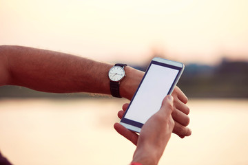 Man checking time on his wrist watch and using cellphone outdoors.