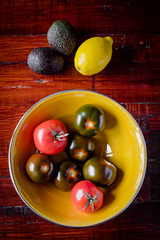 Selection of organic tomatoes in a yellow bowl on wooden background.