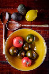 Selection of organic tomatoes in a yellow bowl on wooden background.