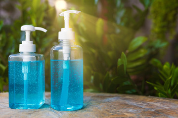Blue alcohols gel bottle on blur green nature background and sun ray. Hand sanitizer gel in pump bottle. With copy space for text or design. Blue alcohols gel on wood table. 