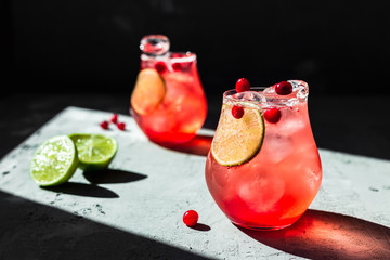 Cranberry tonic with lime in beautiful glasses, grey background, direct natural light, horizontal photo - obrazy, fototapety, plakaty