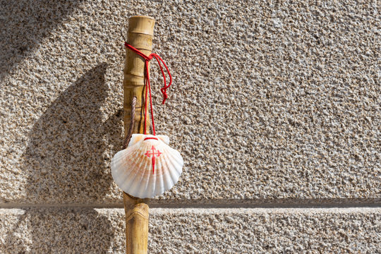 Walking stick and seashell of the Camino de Santiago leaning on granite stone wall. Santiago de Compostela pilgrimage concept