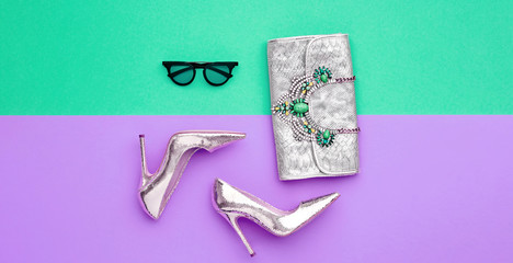 Fashion accessories minimal flat lay. Shoes heels, trendy handbag clutch. Pop art concept. Woman fashionable accessories on purple green, top view, banner. Creative design color