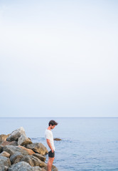 Young caucasian man with his hands in his pockets on a stone pier in the sea