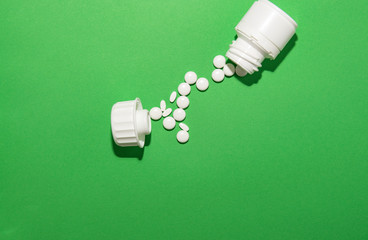 White pills poured from the packaging lie a path from the jar to the lid