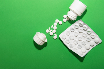 White pills poured from the packaging lie a path from the jar to the lid with a package of medicines