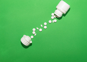 White pills poured from the packaging lie a path from the jar to the lid