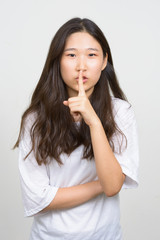 Portrait of young beautiful Asian woman with finger on lips