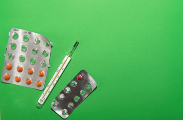 thermometer and packaging with pills lie on a green background