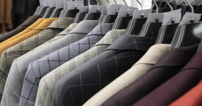 Menswear classical different suits on hangers in row in clothing shop in mall. Lots of costumes on rack in store. Business and retail concept.