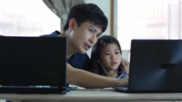 Asian father help little daughter learning at home watch video on modern laptop, smiling, little girl child using computer do homework. online student classroom concept.