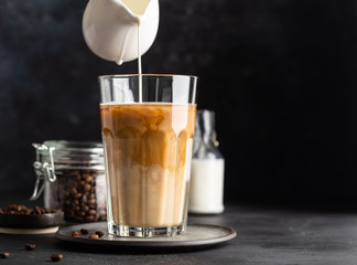 Coffee latte in glass, coffe beans in glass jar and a bottle of milk or cream. Soft drink, refreshing beverage. Dark background. Copy space.