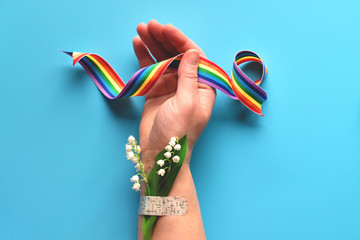 Thank you doctors and nurses! Rainbow ribbon in hand of mature woman with chamomile flower and grass bouquet attached with medical aid patch. Creative modern flat lay, top view on blue background.