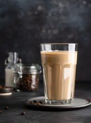 Coffee latte in glass, coffe beans in glass jar and a bottle of milk or cream. Soft drink, refreshing beverage. Dark background. Copy space.
