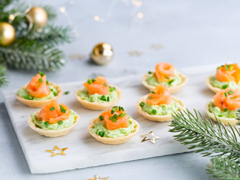 Holiday appetizer canapes with salmon avocado cream cheese on a light background with Christmas decorations. Festive table recipe ideas for New Year's and Christmas holidays.