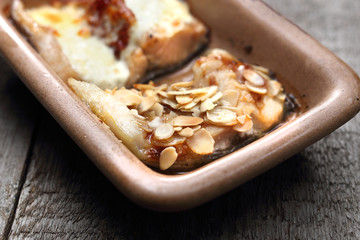 Carp baked with almonds, cheese and dried tomatoes. Appetizing homely dish on a wooden table.