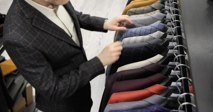 Elegant young businessman is shopping choosing office suit in clothing store, top view. Man making purchases and buying. Lots of costumes on hanger in shop. Classical suits and jackets.